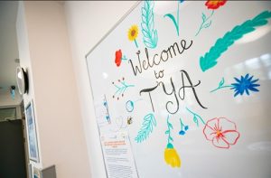 A whiteboard shows a colourful design saying 'Welcome to Teenage and Young Adults' in Bristol's Oncology centre.